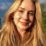 A woman with long, blonde hair smiles at the camera in the sun.