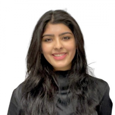 A woman with long, black hair wearing a black, long sleeve smiles at the camera in front of a stark white background.