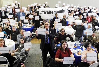 A group of people hold signs that read "#WeRemember"
